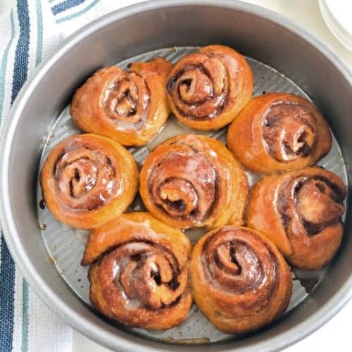 "cinnamon rolls" in round metal cake pan next to white kitchen towel with dark and light blue stripes