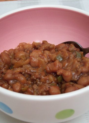 Easy Baked Beans in round bowl with polka dots and pink inside on striped ream place mat with spoon