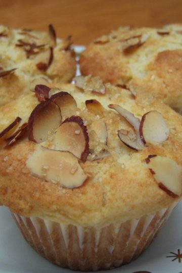 Lemon Ricotta Muffins topped with slivered almond on small white plate with gold stars and swirls