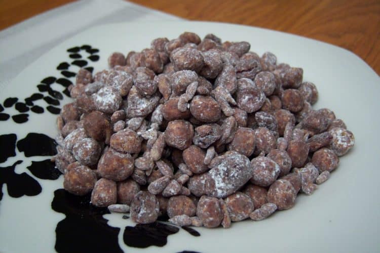 Monkey Mix peanut butter captain crunch cereal, chocolate chips, dried cranberries, whole almonds, coated in powdered sugar in a square bowl with black flowers on striped cream place mat