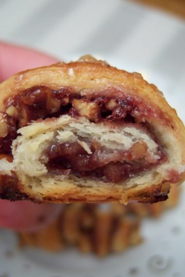 Rugelach with raspberry jam and walnuts bite taken out with small white plate with gold stars and swirls in background