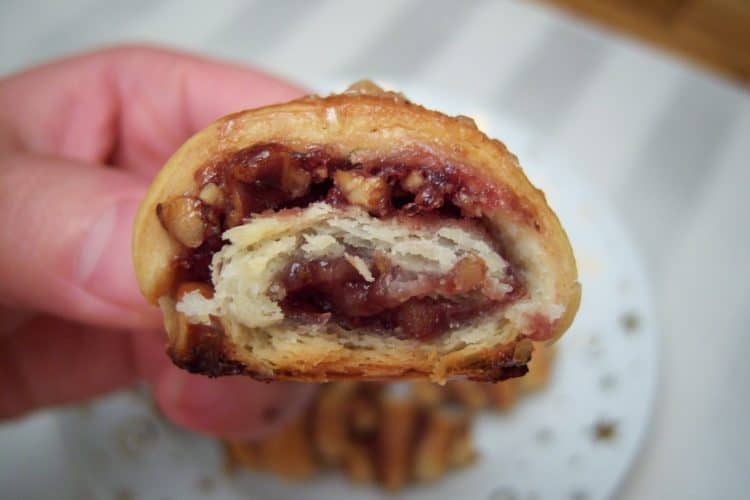 Rugelach with raspberry jam and walnuts bite taken out with small white plate with gold stars and swirls in background