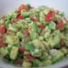 Fresh Guacamole with tomatoes, garlic, onion in white round bowl with black flowers
