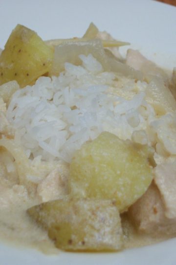 Thai red curry over rice with chicken, potatoes and onion in a white square bowl