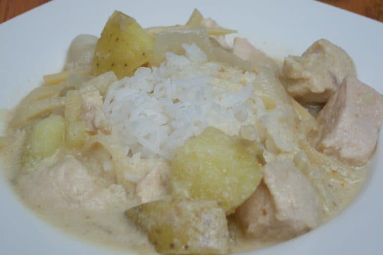 Thai red curry over rice with chicken, potatoes and onion in a white square bowl