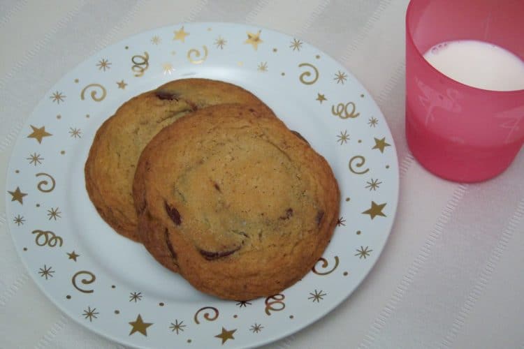 The Famous NY Times Chocolate Chip Cookies on small round plate with gold stars and swirls on striped cream place mat with plastic pink cup filled with milk