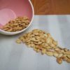 Roasted Pumpkin Seeds in pink bowl spilled on white striped place mat