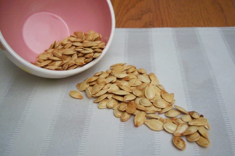 Roasted Pumpkin Seeds in pink bowl spilled on white striped place mat