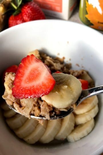 Baked apple oatmeal in square glass baking dish with sliced strawberries and bananas on a square white plate
