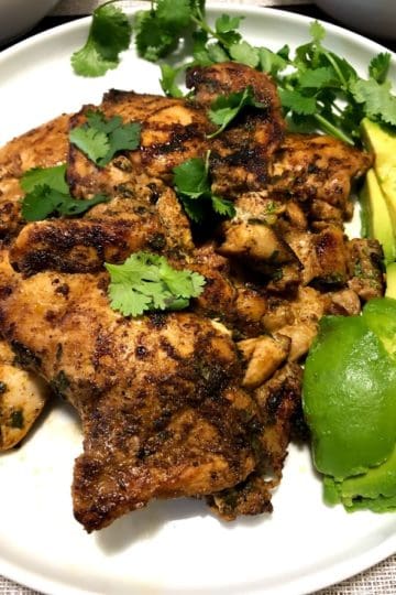 Cilantro lime chicken thighs on white plate with cilantro and avocado slices