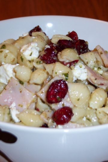 Amy's pesto pasta salad with turkey lunch meat, dried cranberries, pesto, shell pasta, mayo and goat cheese in round bowl with black flowers