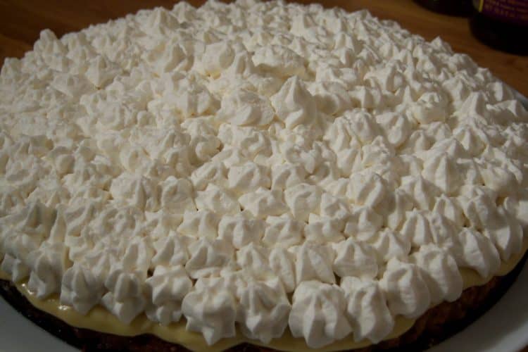 Banana cream pie with piped whip cream on large round plate