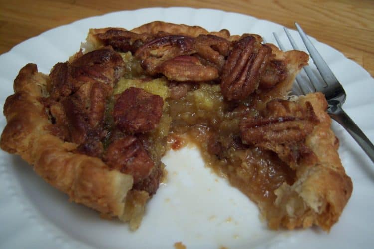 Small pecan pie sliced on white plate with fork