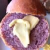 Purple sweet potato roll on white plate split open with pat of butter