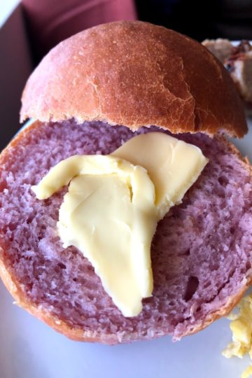 Purple sweet potato roll on white plate split open with pat of butter