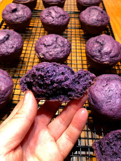 Hand holding a purple sweet potato muffin broken in half with sweet potato muffins on a cooling rack in the background