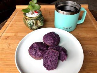Purple sweet potato muffins on a round white plate on a cutting board next to a coffee mug