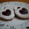 Heart shaped Linzer Sables with raspberry jam on small white plate with gold stars and swirls