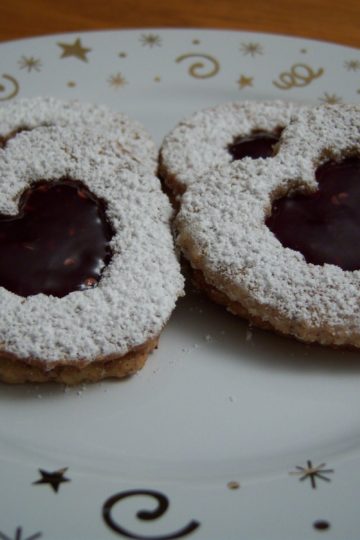 Heart shaped Linzer Sables with raspberry jam on small white plate with gold stars and swirls