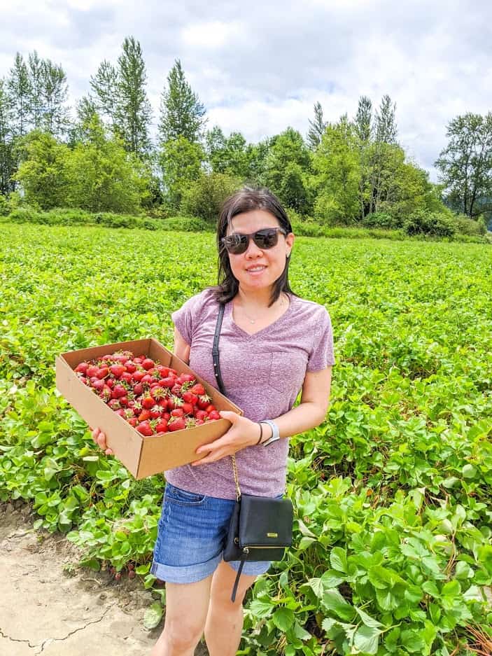 Lady holding a cardboard box of strawberries in a strawberry patch