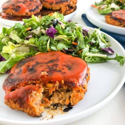 Turkey veggie meatloaf patty on round white plate with a green salad, round white plate in the background with additional turkey veggie meatloaf patties.