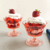 Mini strawberry shortcake trifles with purple sweet potato biscuits in pink vintage footed dessert glasses with sliced strawberries, cool whip, biscuits and whole strawberry on top of cool whip, blue dish towel