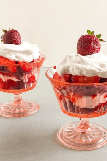 Mini strawberry shortcake trifles with purple sweet potato biscuits in pink vintage footed dessert glasses with sliced strawberries, cool whip, biscuits and whole strawberry on top of cool whip, blue dish towel