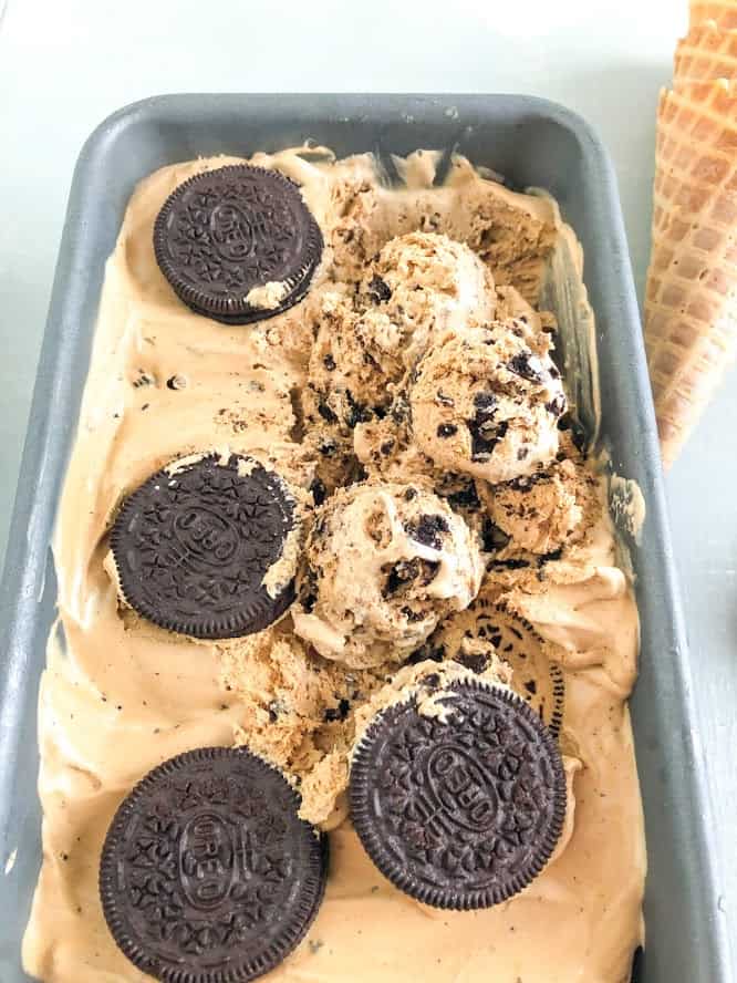 Ice cream topped with whole Oreo's in a metal loaf pan with waffle cone in the background
