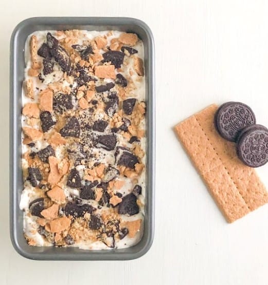 Frozen loaf pan of ice cream topped with Oreo's and graham cracker pieces. Whole sheet of graham cracker and two whole Oreo's on the side.