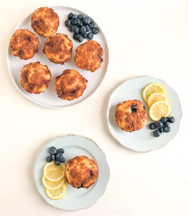Lemon blueberry muffins on small round light blue plates with lemon slices and blueberries, round white medium plates with additional muffins and blueberries