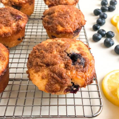 Lemon blueberry muffin on silver metal wire cooling rack next to blueberries and lemon slices