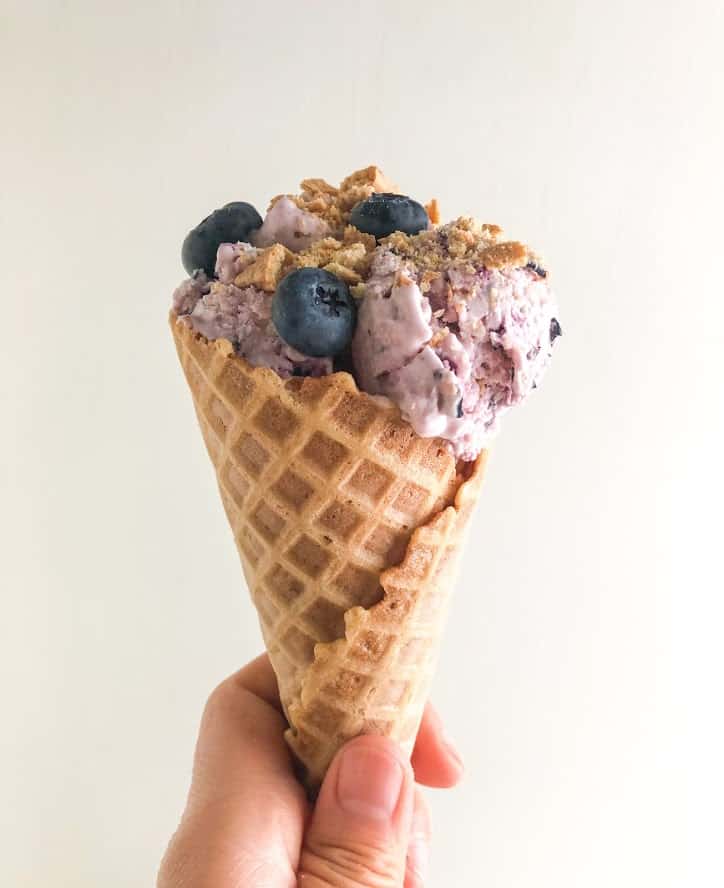 hand holding waffle cone with no churn ice cream topped with blueberries and graham cracker pieces
