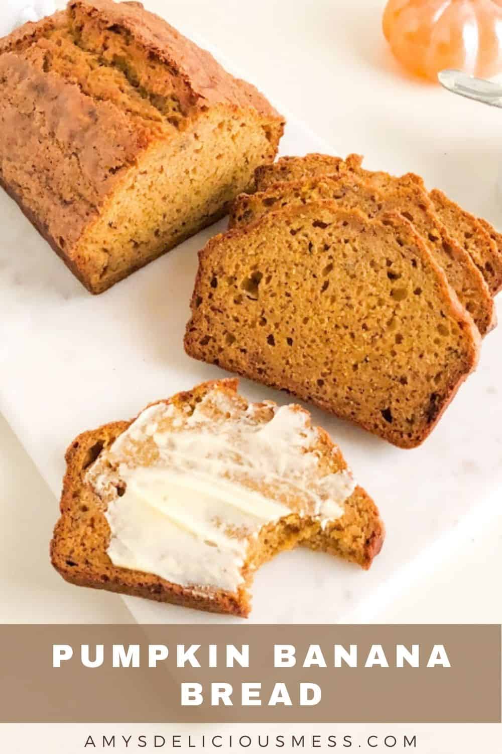loaf of pumpkin banana bread with slices and buttered slice with bite taken out on marble cutting board. Next to small round white ramekin of butter with silver butter knife, with orange glass pumpkin behind.