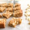 blondie bars on parchment paper one with bite taken out, macadamia nuts next to blondies, ramekins of white chocolate chips and macadamia nuts in the background