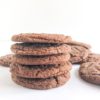 Stack of molasses cookies with cookies on parchment paper next to it.