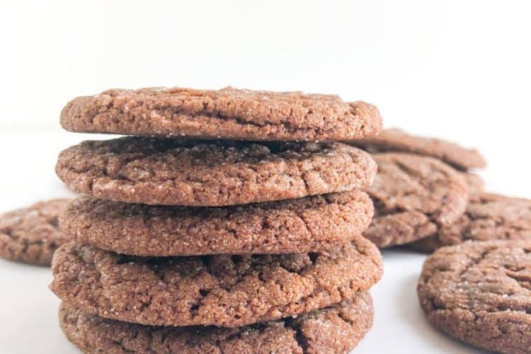Stack of molasses cookies with cookies on parchment paper next to it.