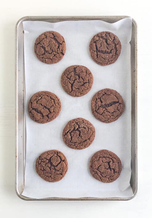 Baked molasses cookies on parchment lined baking sheet.