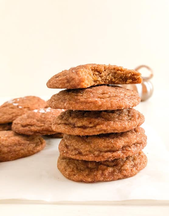 Stack of pumpkin cookies on parchment paper with additional cookies  and silver pumpkin in the background.