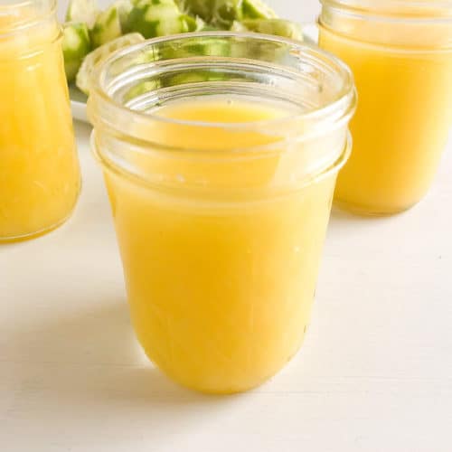 Cooked lime curd in 3 glass mason jars, lime halves in the background on a round white plate.