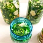 Sliced jalapenos and smashed garlic in mason jars, two clear quart and one blue pint jar.
