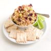 Medium white round plate with plain crackers and celery sticks with small bowl of chicken salad in the middle. Extra cranberries and cashews on top of the chicken salad with a small silver cocktail spoon.