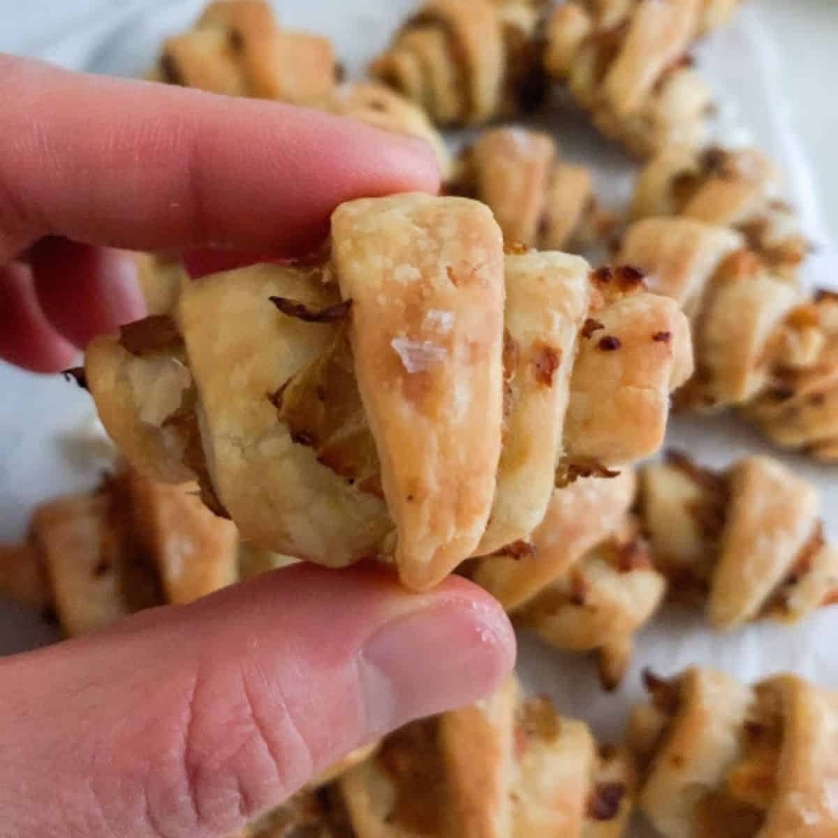 Hand holding baked rugelach with additional rugelach in the background on parchment paper.