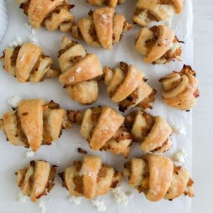 Baked rugelach arranged on top of and next to each other on parchment paper with crumbles of feta for decoration.