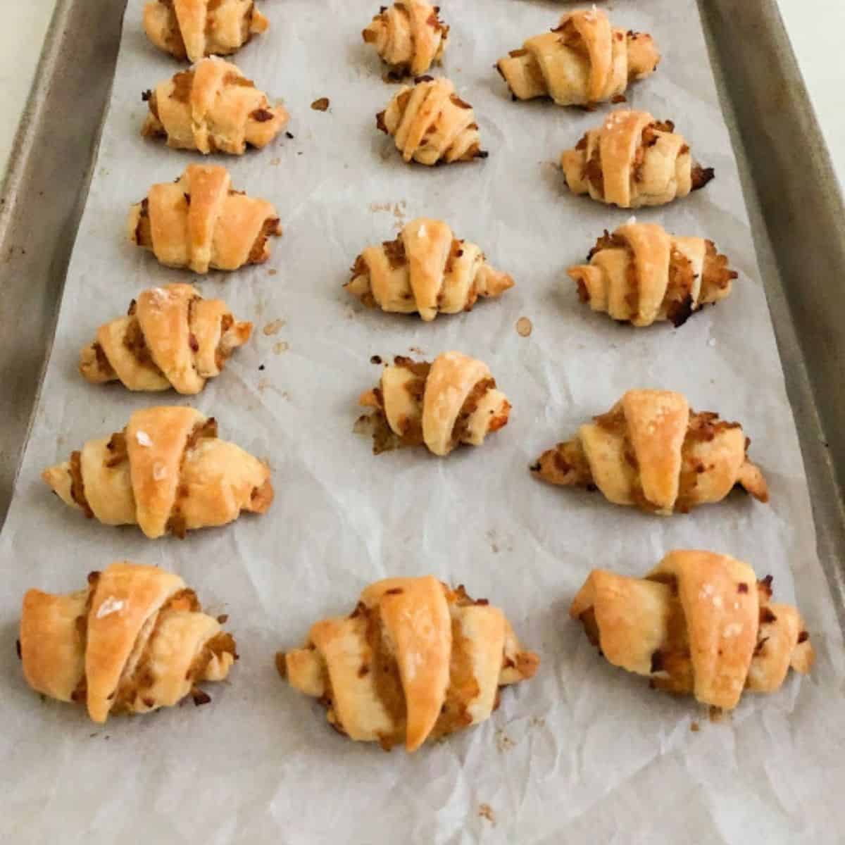 Baked rugelach on metal USA pan small sheet pan lined with parchment paper.