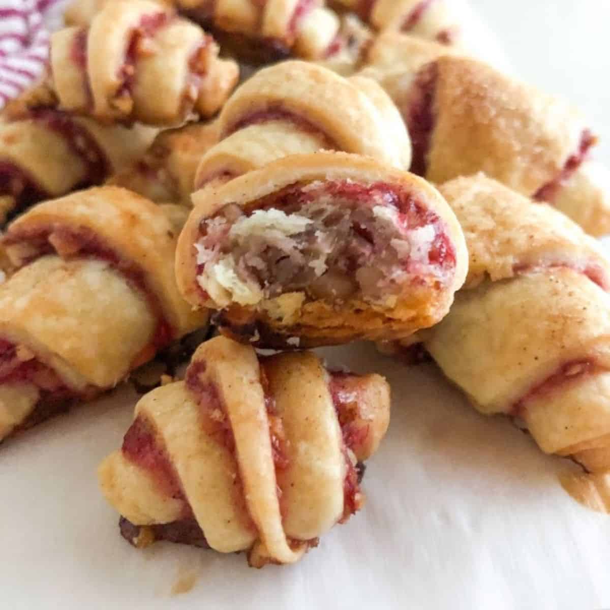 Baked rugelach arranged on parchment paper with one bite taken out of rugelach on top.