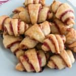 Bake rugelach on light blue round plate with prink and white stripped kitchen towel in the background.