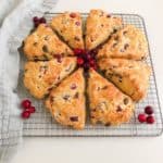 Baked scones on silver metal cooling rack with fresh cranberries as decoration. Light gray linen napkin next to scones for decoration.