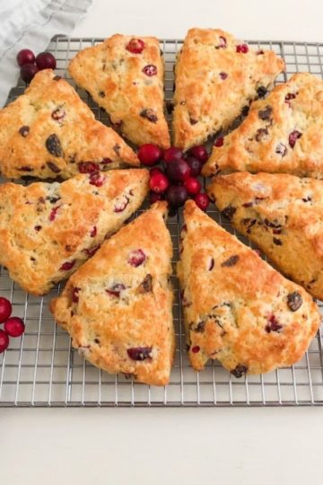Baked scones on silver metal cooling rack with fresh cranberries as decoration. Light gray linen napkin next to scones for decoration.